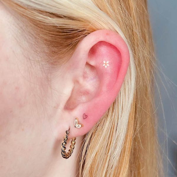 Tiny flower and heart ear tattoo by @bro_tattooing