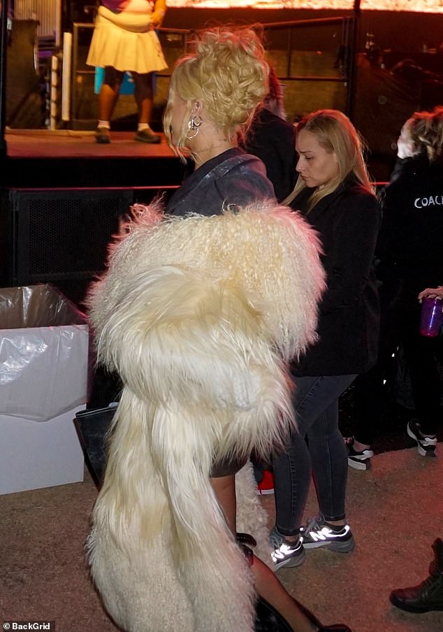 She added a thigh-skimming black leather skirt to the look and had on a navy distressed hoodie under the beige fur