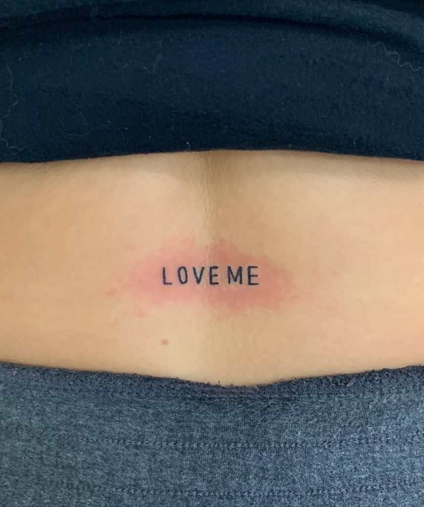 'LOVE ME' Text Lettering Lower Back Tattoo: Bold Affirmation
