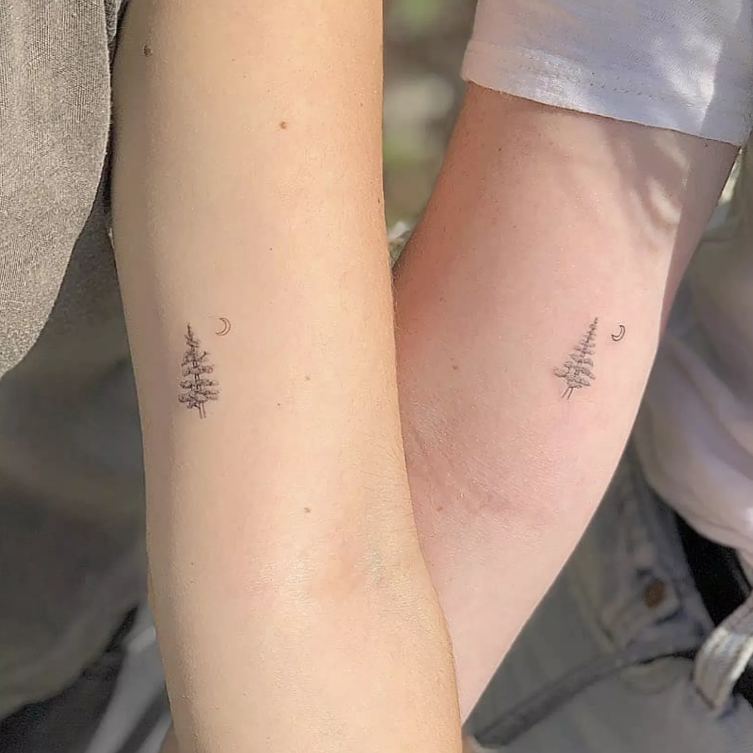 Friends with matching tattoos of a pine tree and crescent moon on upper arm